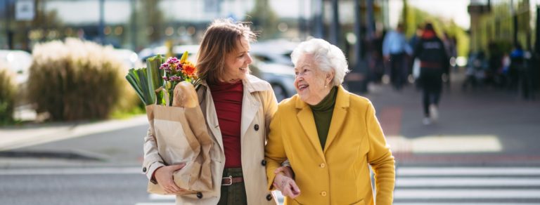 mature granddaughter carrying groceries out to her grandmother's car. senior woman shopping at the shopping center, needing help loading groceries into car.